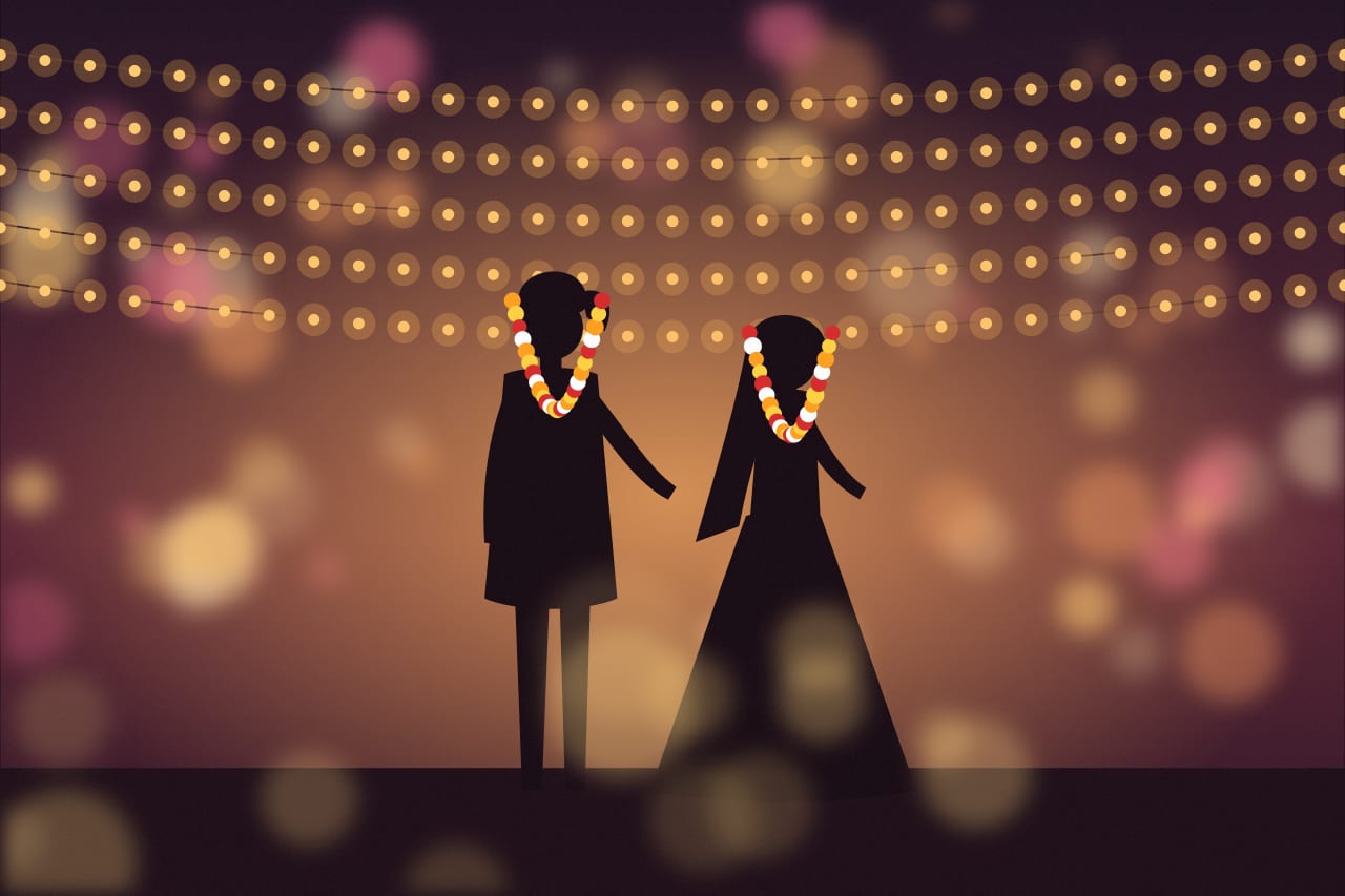 The couple exchanging garlands under string lights